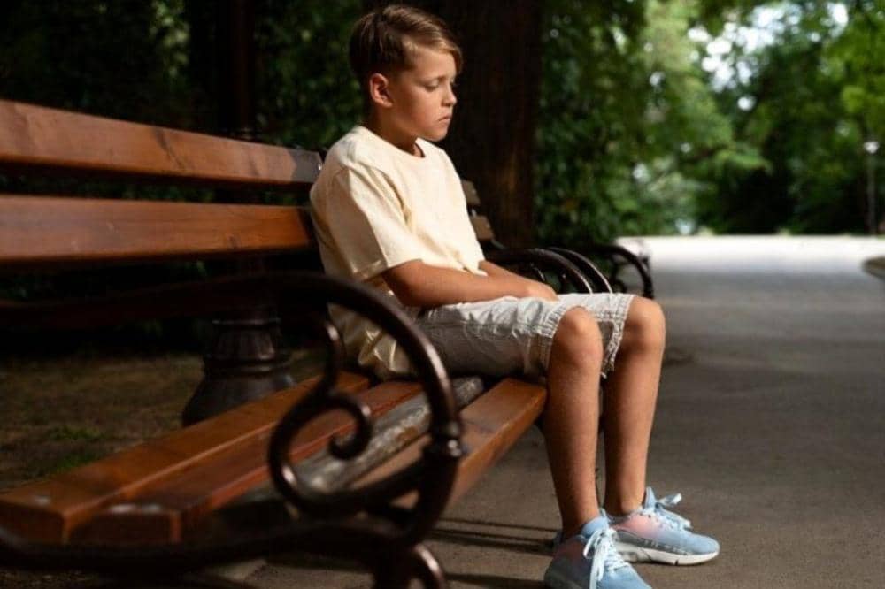 Anak duduk sendiri di bangku taman