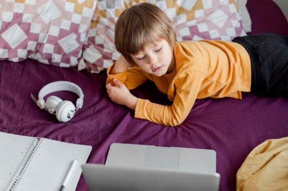 Anak laki-laki bermain laptop di kasur