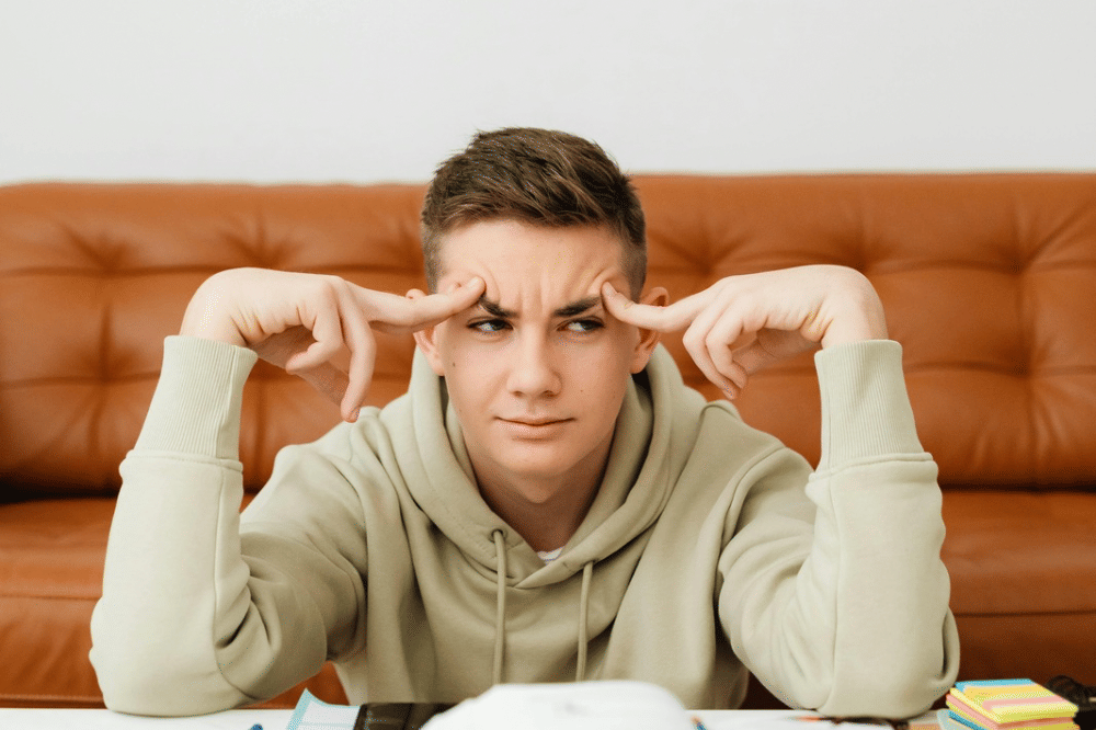 Seorang remaja memegang dahi dengan jarinya dan terlihat bingung 