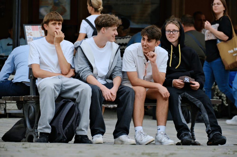 Sekumpulan anak remaja duduk di pinggir jalan sembari berbincang 