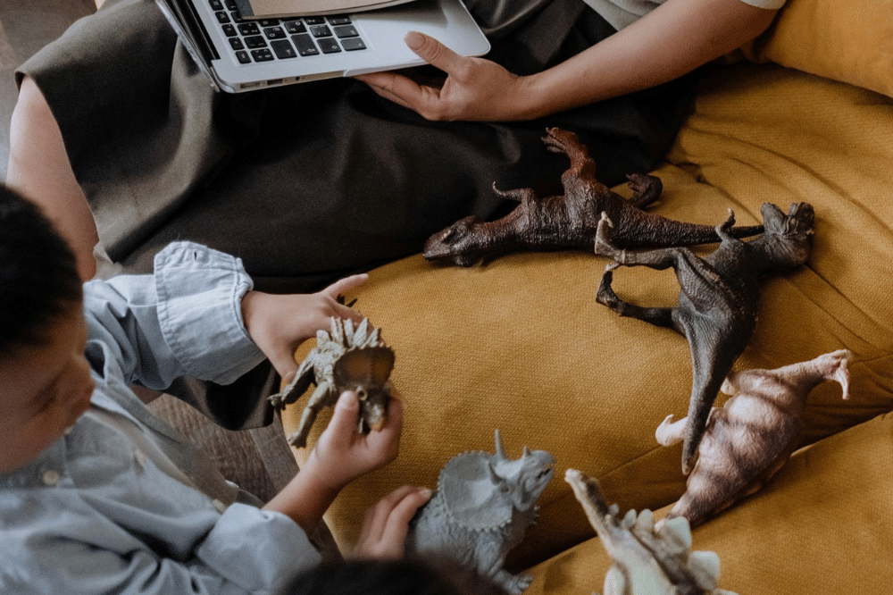 anak-anak sedang bermain mainan dinosaurus di samping orangtuanya yang bekerja