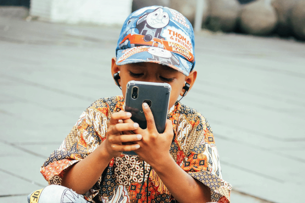 Seorang anak laki-laki sedang bermain handphone dan menggunakan earphone