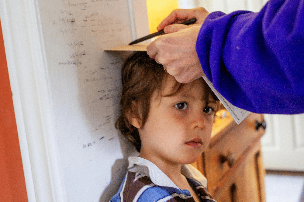 seorang anak yang sedang diukur tinggi badannya di tembok