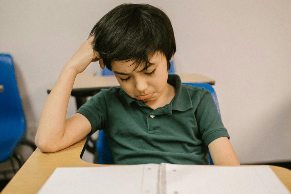 seorang anak laki-laki yang terlihat bersedih saat belajar