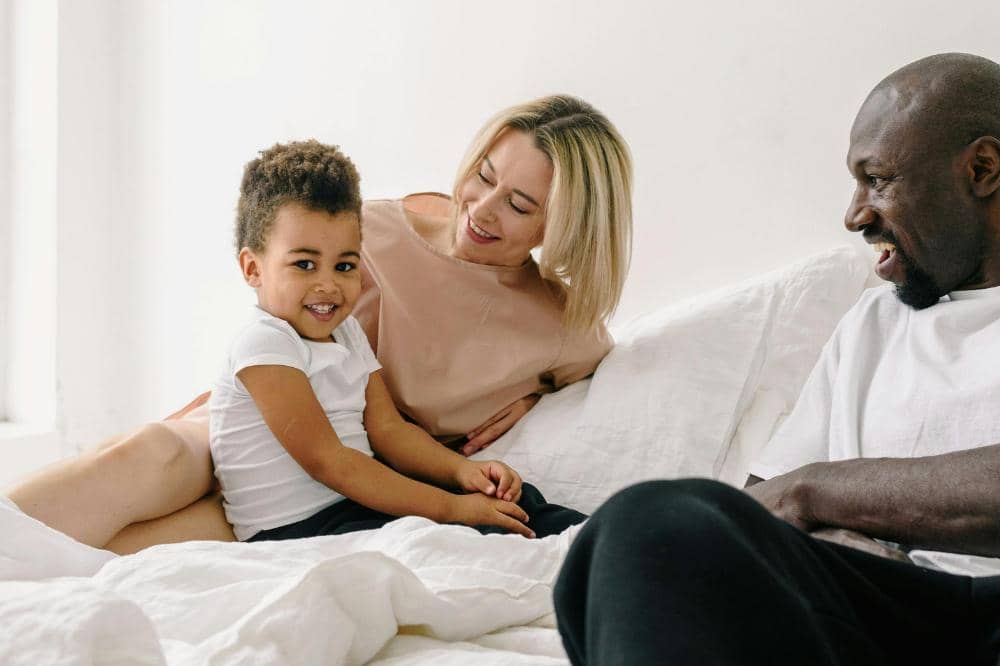 Seorang anak tersenyum duduk di atas tempat tidur bersama orangtua