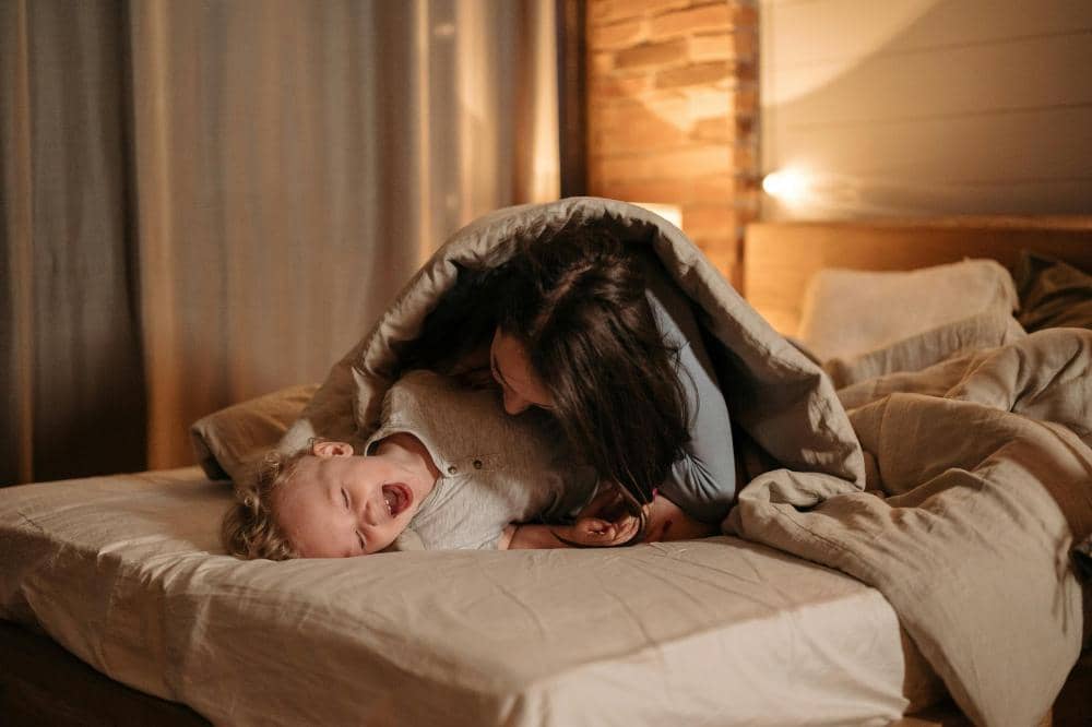 Mama dan anak tertawa bersama di atas tempat tidur