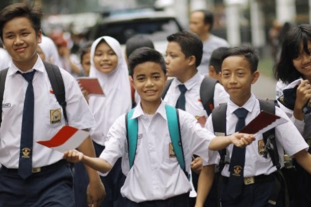 Sekelompok siswa SMP berjalan bersama sambil memegang bendera merah putih.