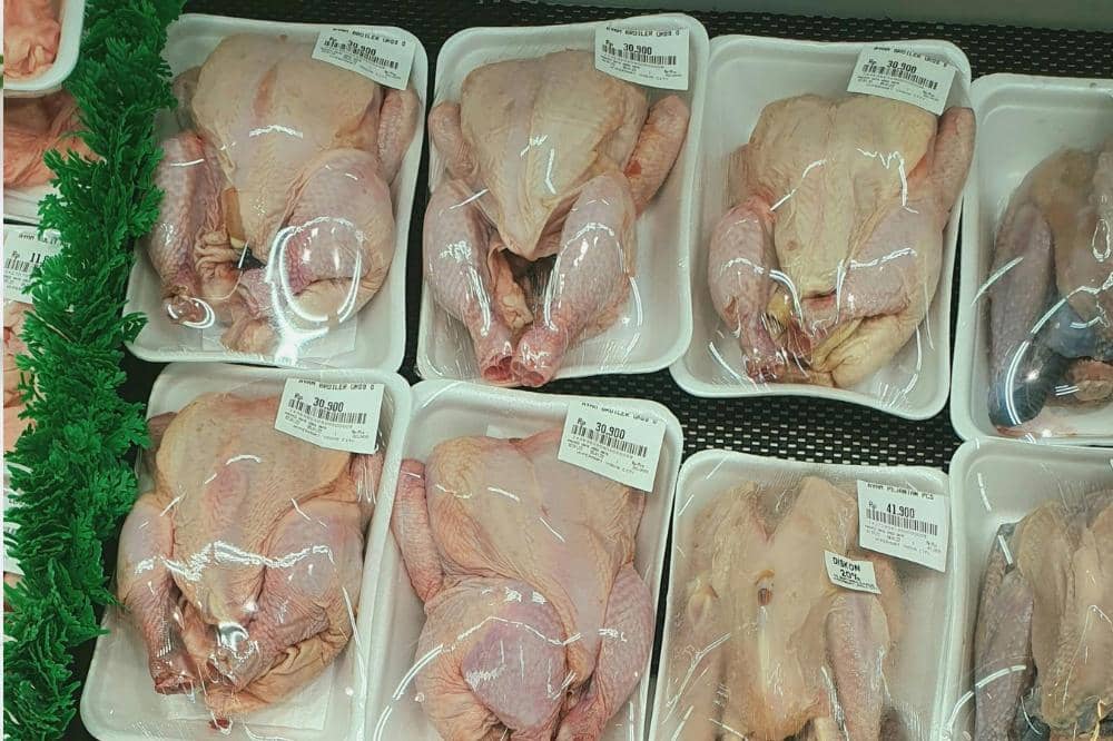 Beberapa ayam utuh mentah dikemas dalam wadah styrofoam dan dibungkus plastik bening dengan label harga di rak pendingin supermarket.