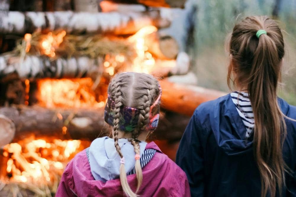 Dua anak perempuan berjaket melihat api unggun besar