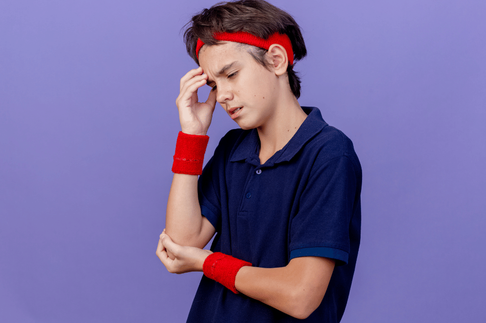 Remaja tampak kesakitan sambil memegang kepala dan siku di latar ungu.