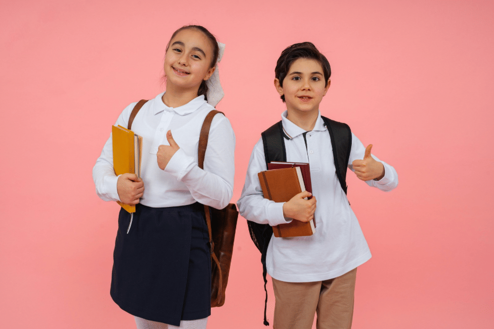 Dua anak sekolah mengenakan seragam putih dengan ransel dan buku di tangan