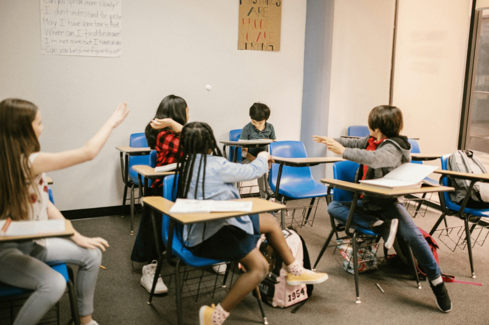 Sekelompok anak duduk di kursi kelas dengan meja belajar