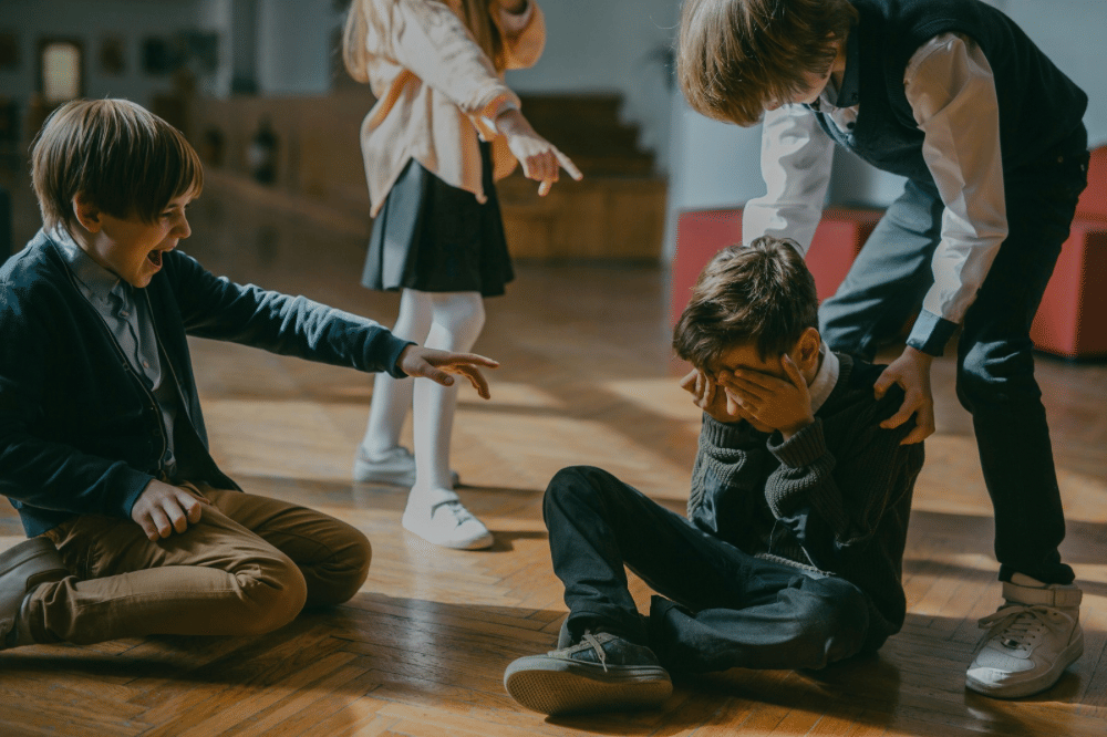 Beberapa anak sekolah mengejek seorang anak laki-laki yang duduk di lantai 
