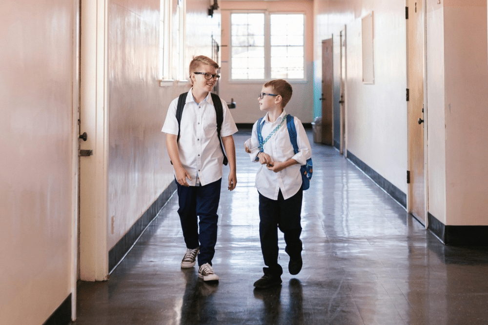 Dua anak laki-laki berseragam sekolah berjalan bersama di lorong sekolah