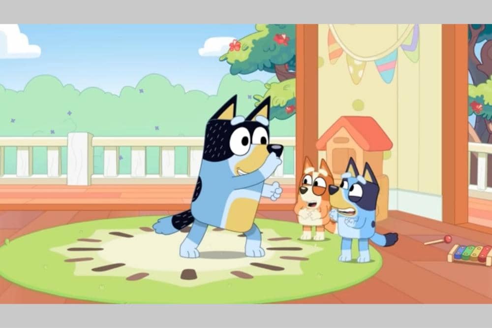 Bluey, Bingo, dan Bandit sedang bermain di ruang bermain dengan latar halaman rumah yang cerah.