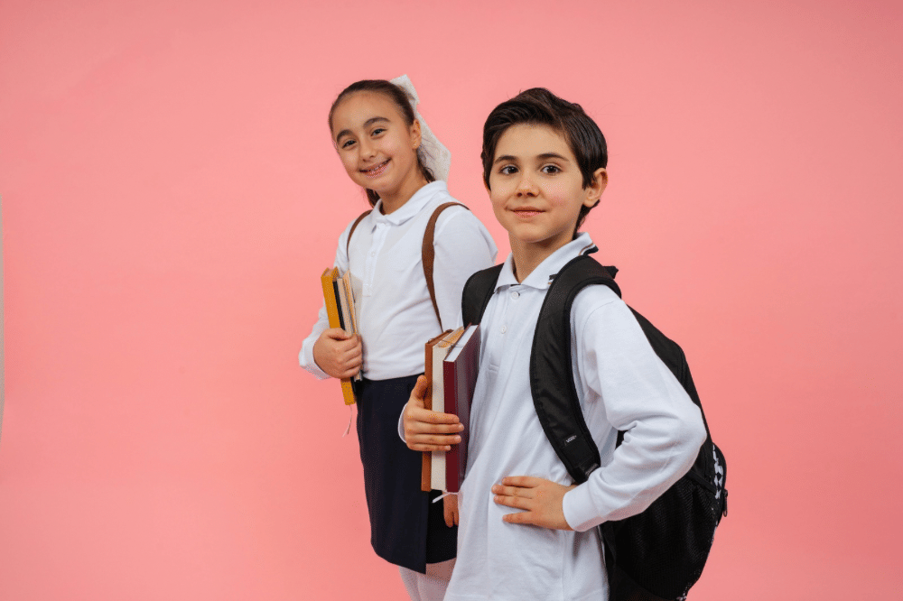 Dua anak sekolah mengenakan seragam putih dan membawa buku