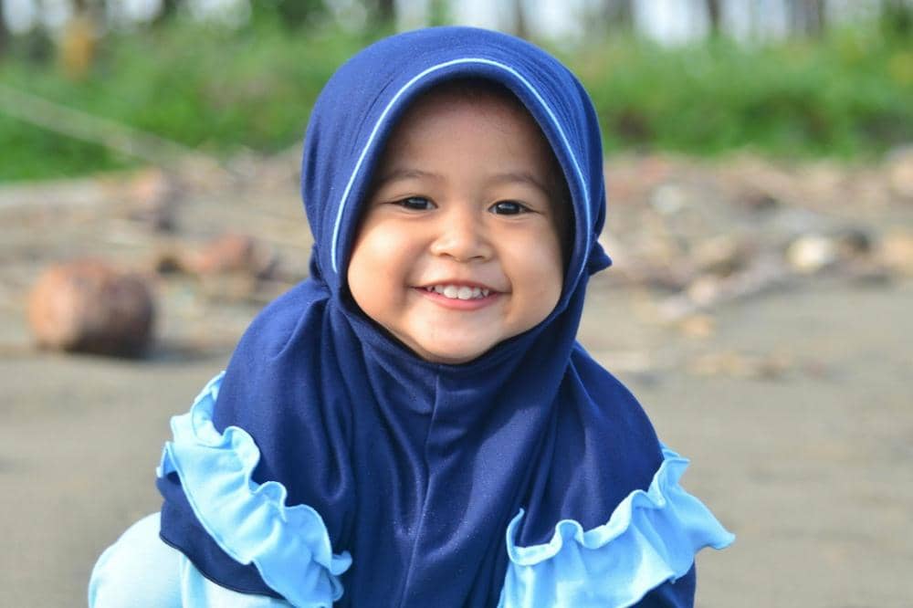 Anak perempuan memakai hijab biru tua tersenyum ceria