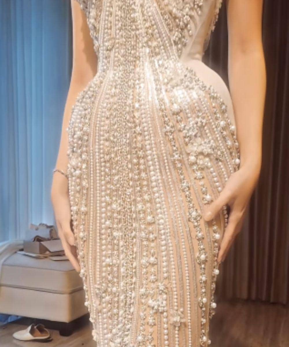 Gaun mewah berwarna nude dengan hiasan mutiara dan kristal yang tersusun rapi membentuk pola elegan di seluruh bagian tubuh.