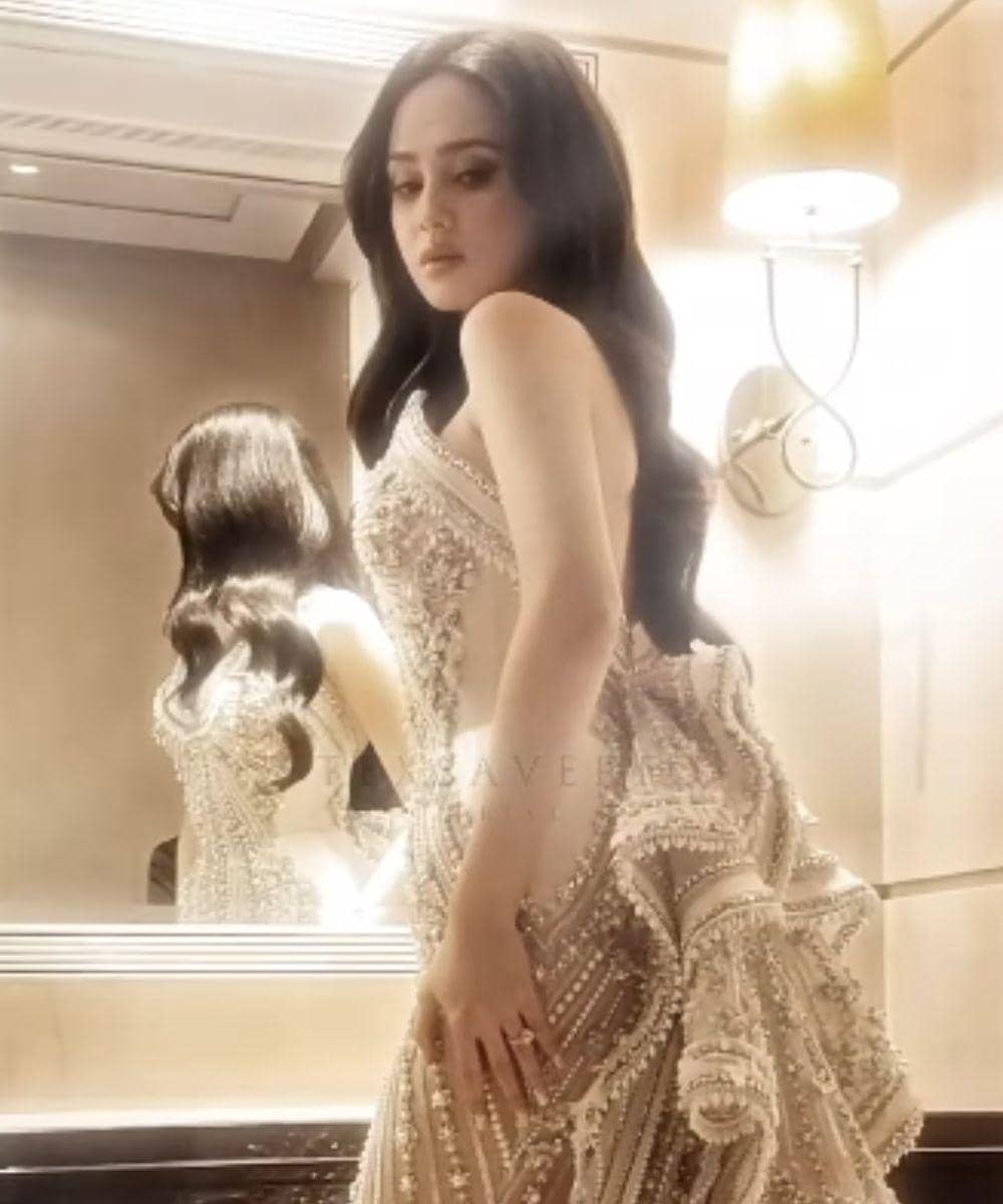 Syifa Hadju berpose di depan cermin mengenakan gaun mewah berwarna krem dengan hiasan manik-manik dan bordir detail di ruangan elegan.
