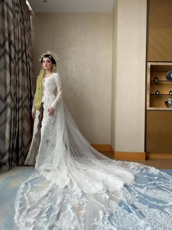 Syifa Hadju mengenakan kebaya pengantin putih berhias renda dan kerudung panjang dengan siger serta ronce melati di rambutnya.