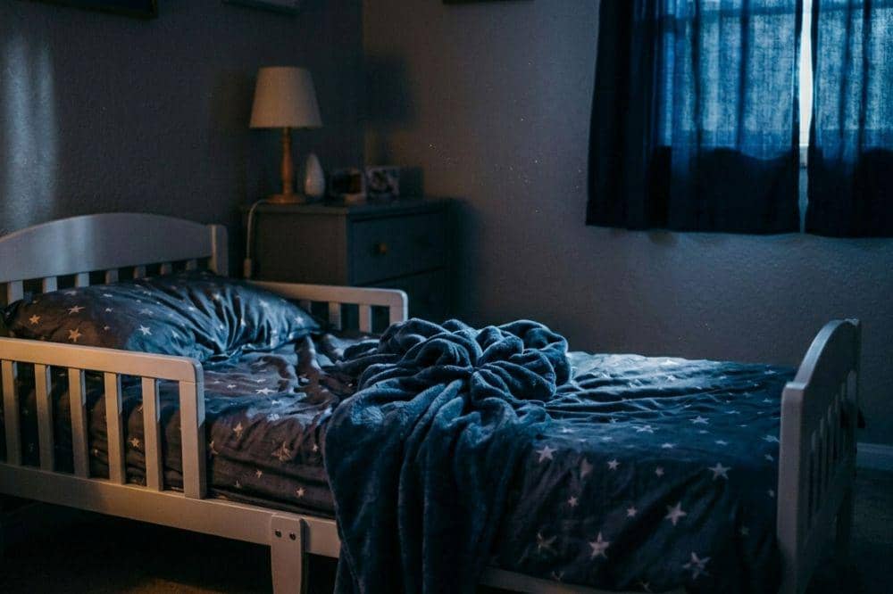 Tempat tidur anak dengan sprei bermotif bintang berwarna biru tua di kamar yang diterangi cahaya lembut dari jendela.