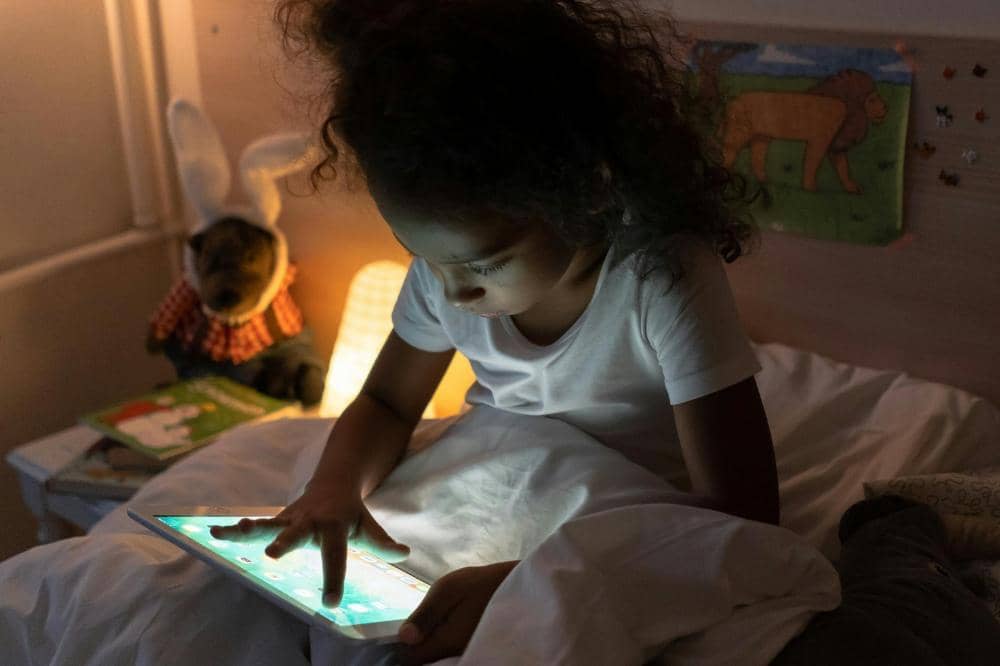 Anak perempuan bermain tablet di kasur