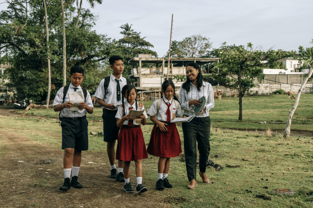 Guru dan murid berjalan bersama sambil membawa buku 