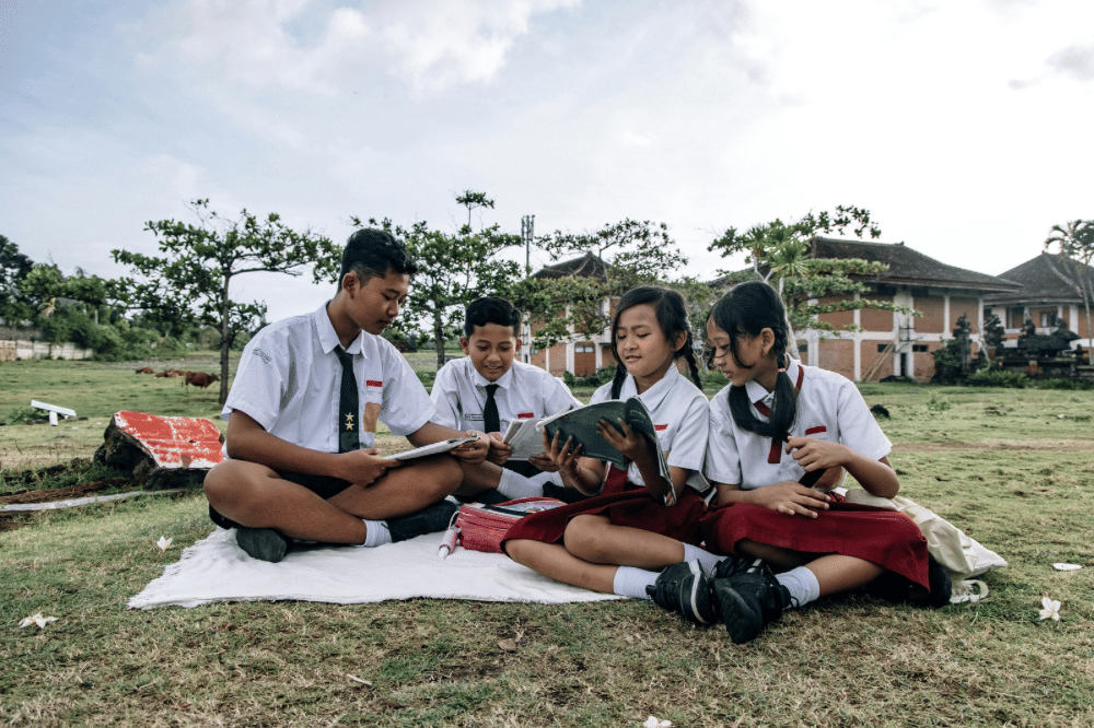 Murid-murid sedang membaca buku bersama di halaman sekolah