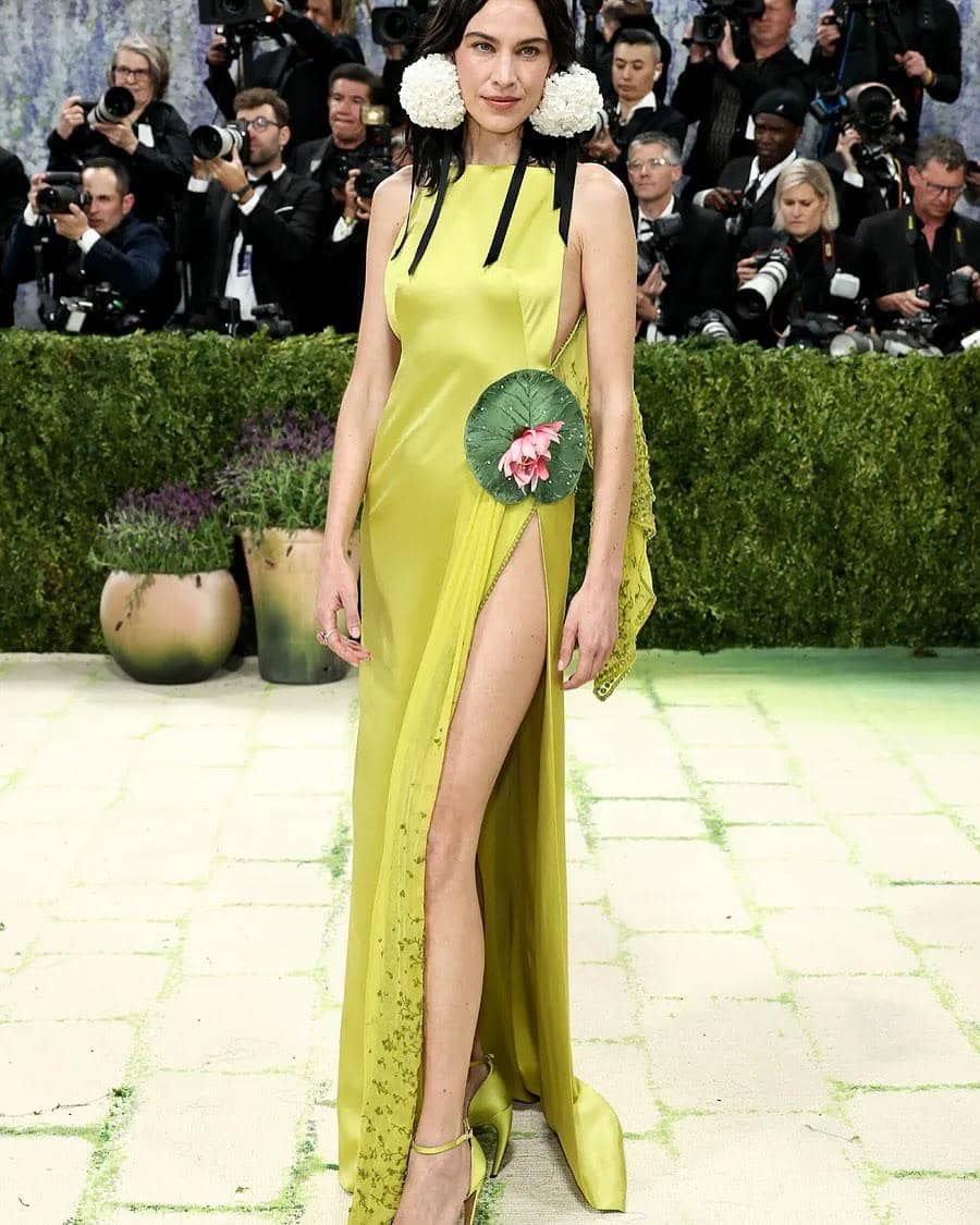 Alexa Chung mengenakan gaun kuning kehijauan dengan belahan tinggi dan hiasan bunga di karpet merah Met Gala