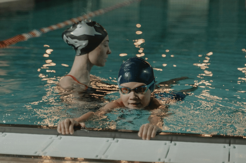 Anak belajar berenang di kolam bersama seorang instruktur