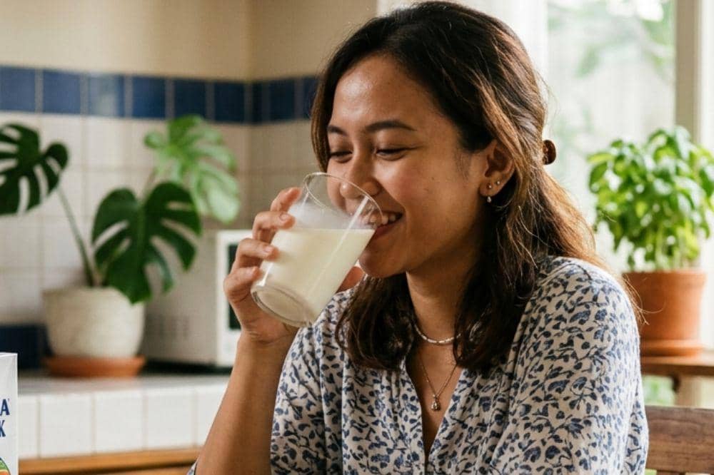 Seorang wanita tersenyum sambil meminum segelas susu probiotik.