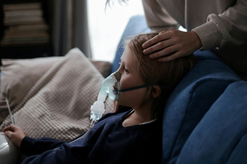 Seorang anak sedang duduk sembari mengenakan alat nebulizer