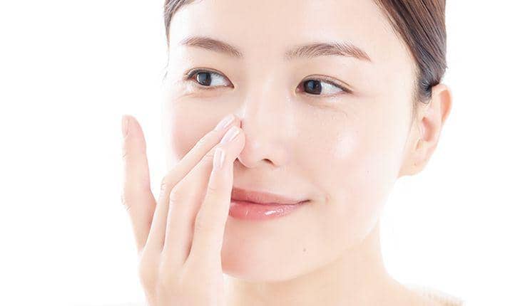erempuan tersenyum natural sambil menyentuh kulit wajahnya yang segar.