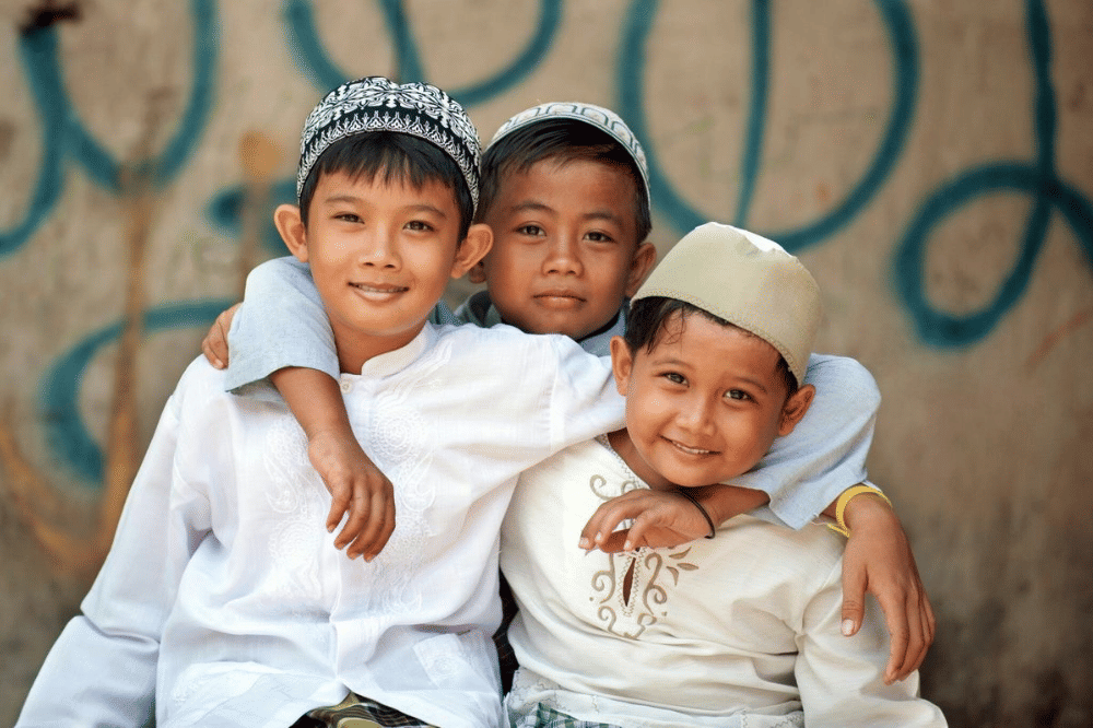 Tiga anak mengenakan peci dan tersenyum 