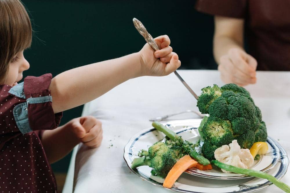 Anak memegang sendoknya sendiri dan memakan sayuran