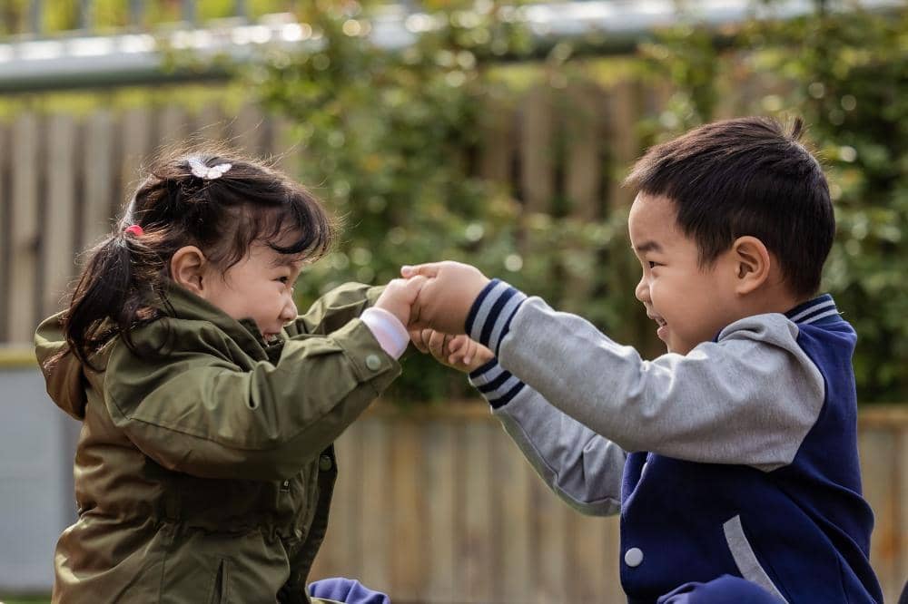Dua anak tersenyum bahagia sambil berpegangan tangan tingkatkan interaksi sosialnya