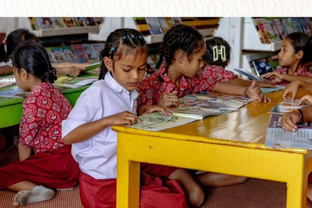 Anak-anak sekolah dasar membaca buku bersama di perpustakaan.