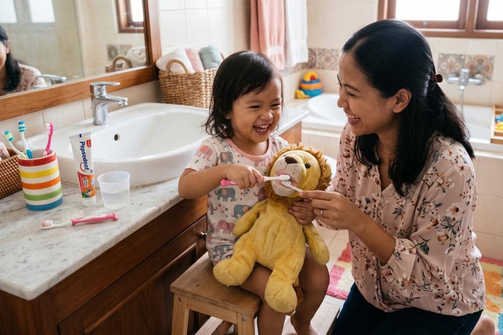 Anak bersama Mama sedang bermain peran menyikat gigi boneka favorit si kecil