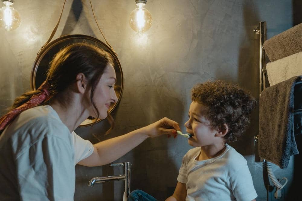 Mama dan anak sedang bergantian menyikat gigi di kamar mandi dengan menyenangkan