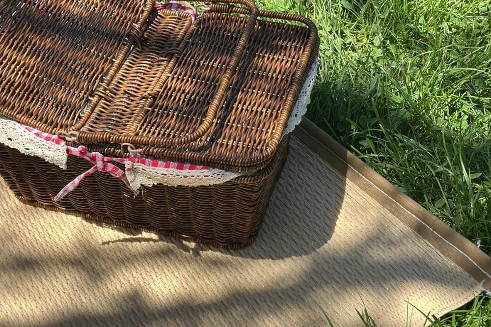 Keranjang piknik cokelat dengan pita di atas kain alas anti air di rerumputan