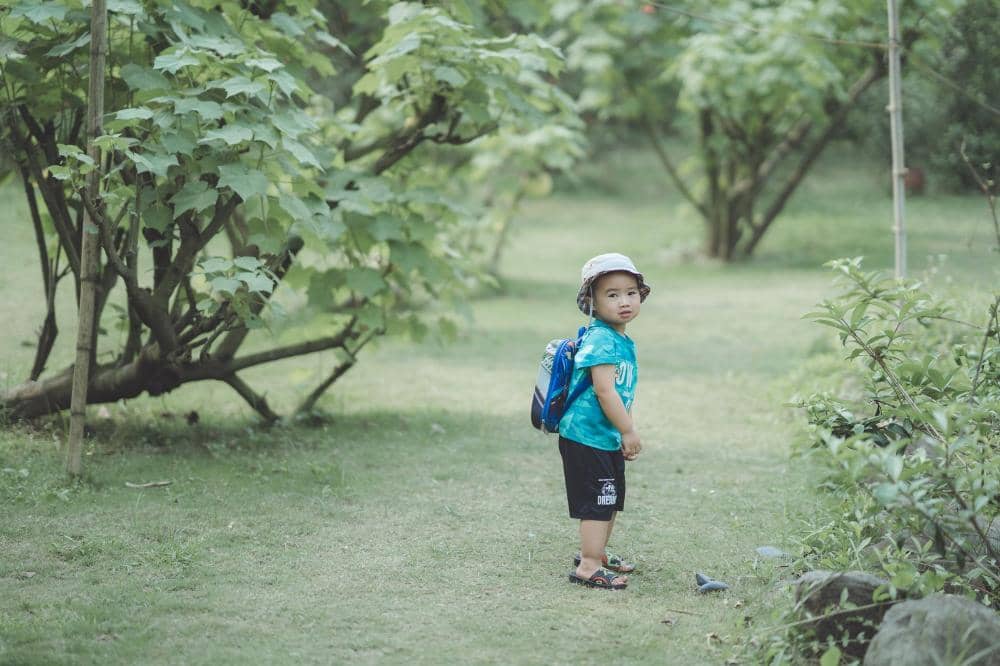 Anak mengenakan topi model bucket hat berdiri di taman