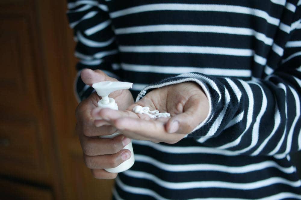 Anak mengenakan sweter garis-garis hitam putih sedang menuangkan lotion ke telapak tangannya