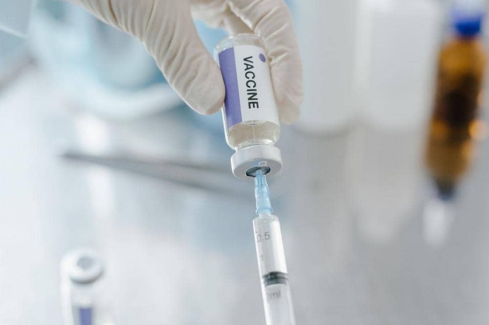 Tenaga medis mengenakan sarung tangan medis sedang menarik cairan vaksin dari botol ke dalam suntikan