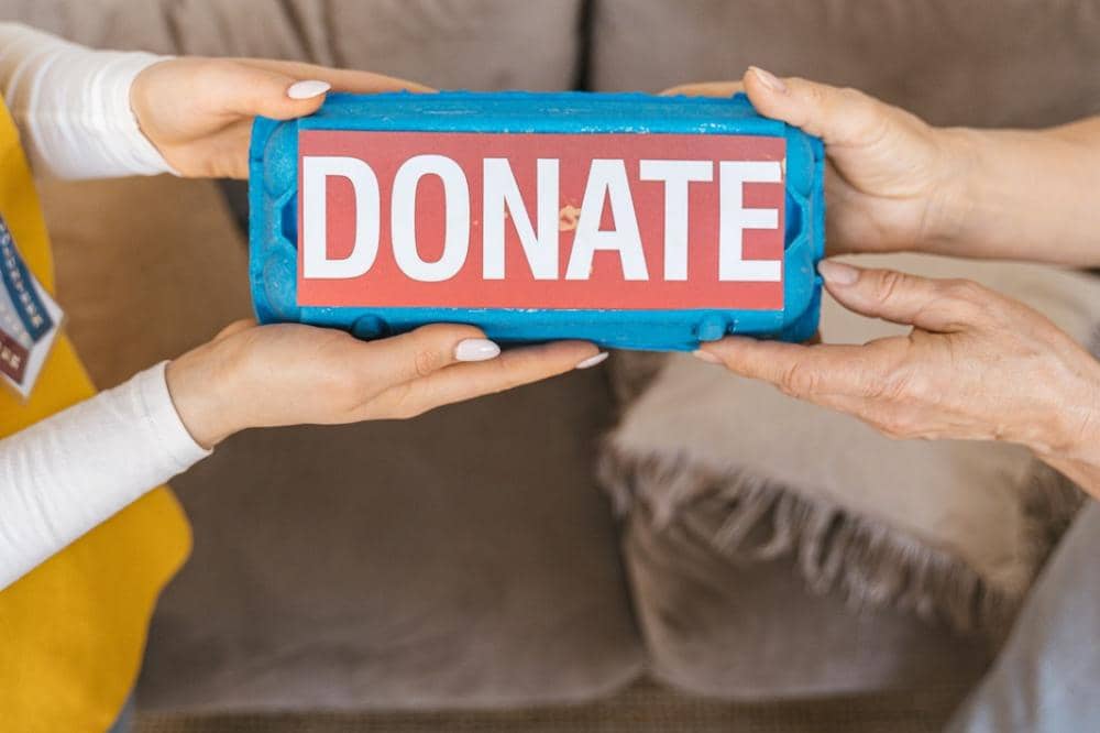 Dua orang saling memegang kotak bertuliskan DONATE sebagai simbol kegiatan donasi dan kepedulian sosial.
