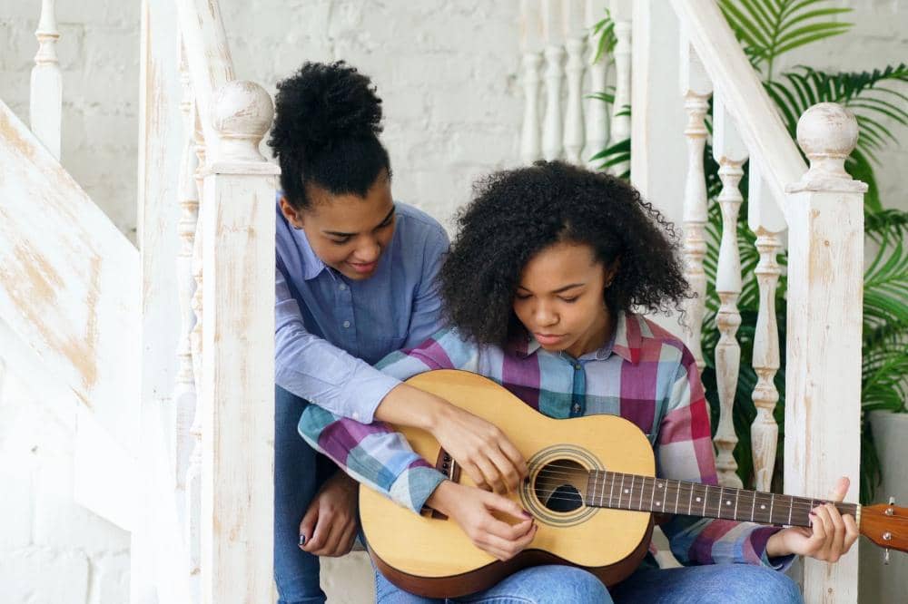 Mama membantu anak bermain gitar untuk menambah rasa percaya dirinya