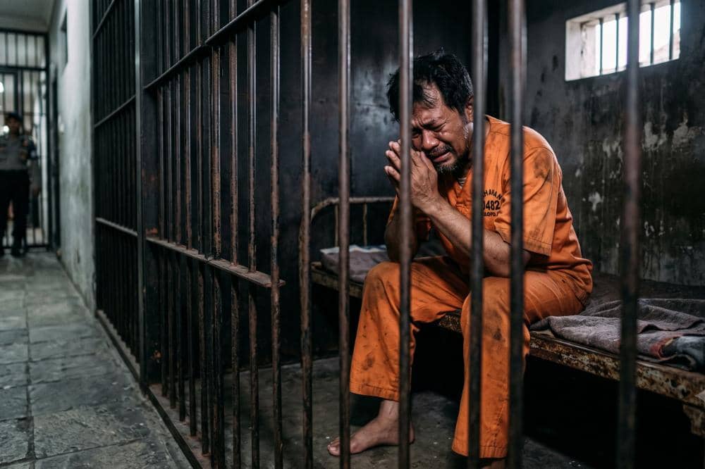 Laki-laki berpakaian tahanan oranye duduk di dalam sel penjara dengan ekspresi sedih