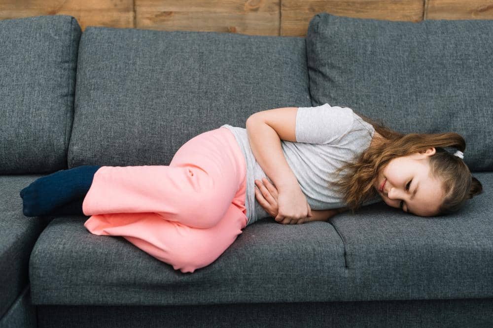 Anak perempuan berbaring di sofa memegangi perutnya sepertinya terkena gangguan pencernaan anak