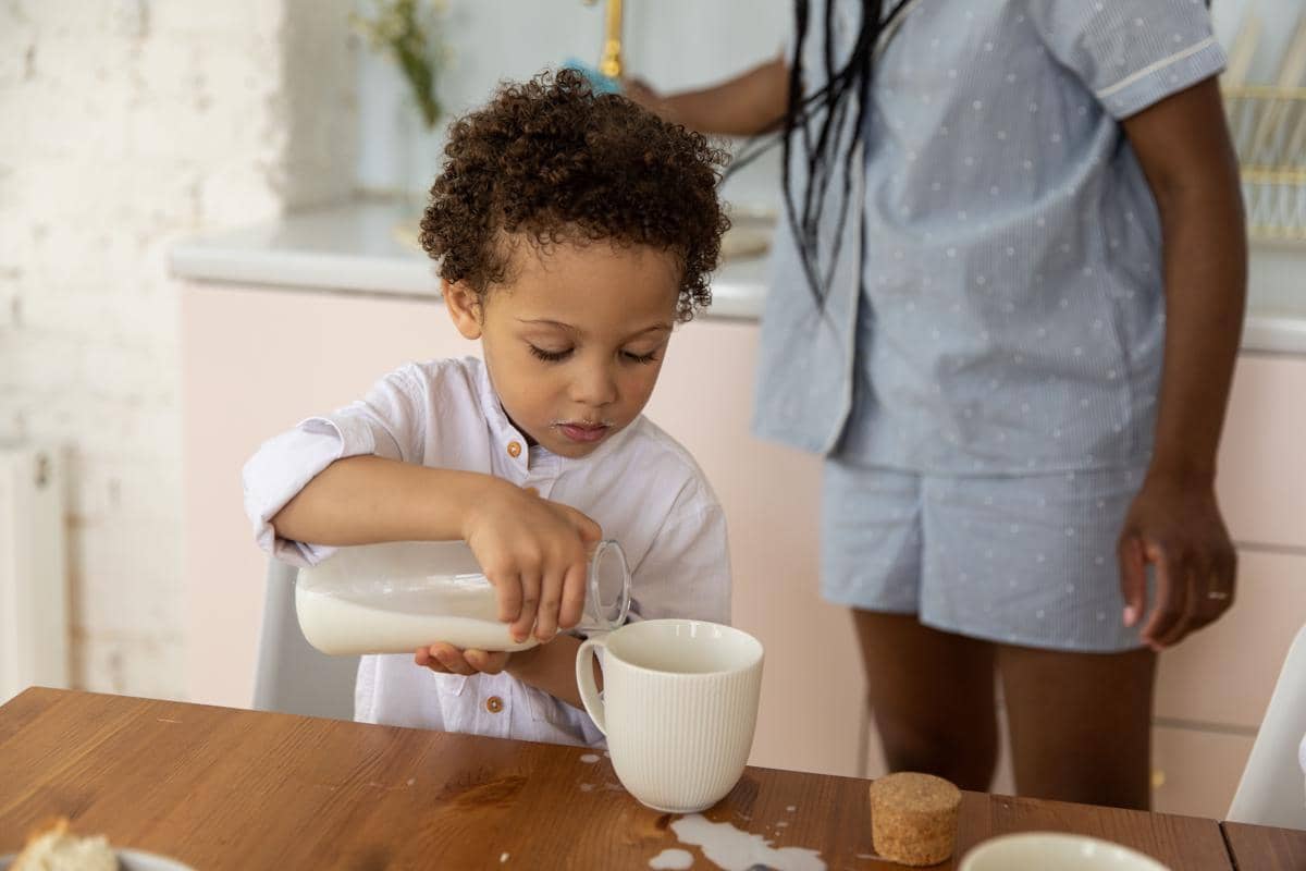 Anak sedang menuang susu ke dalam gelas 