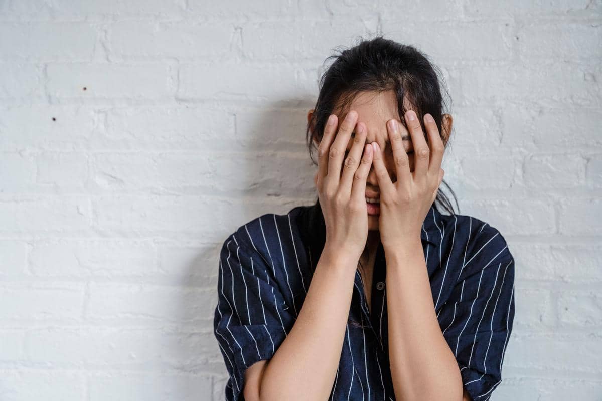 Perempuan dewasa menutup seluruh wajahnya dengan tangan
