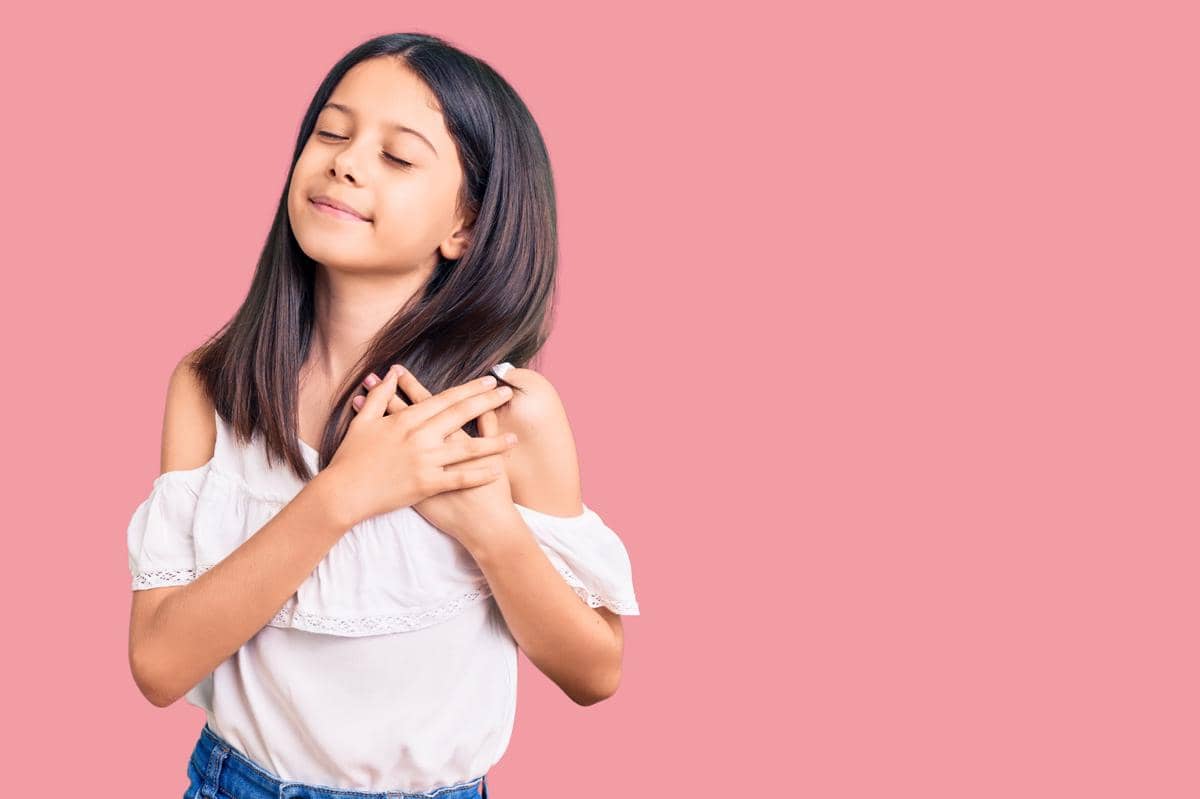 Anak perempuan memberikan gestur menaruh tangan di dekat jantung